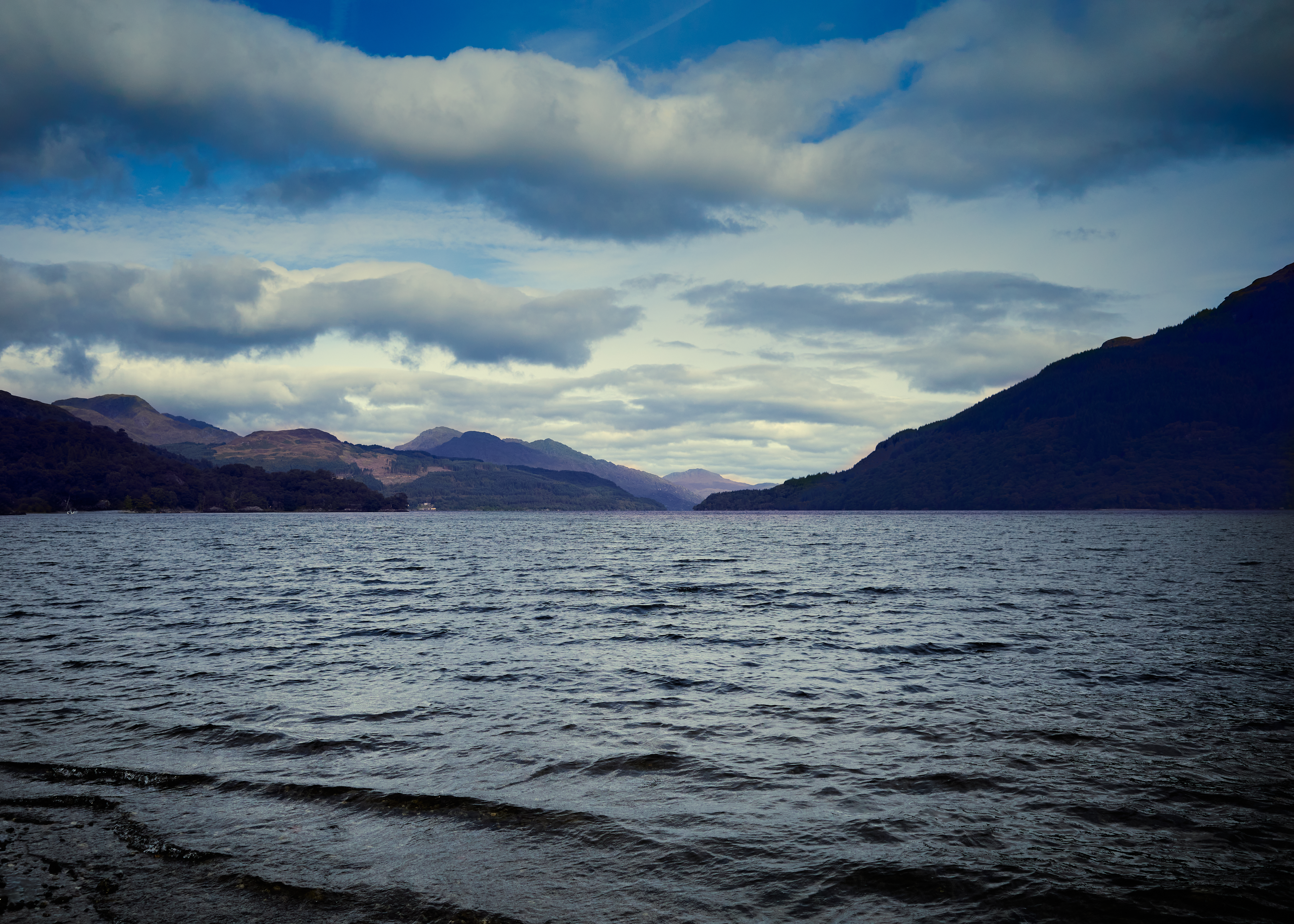 A tranquil lake scene with soft ripples and surrounding mountains.