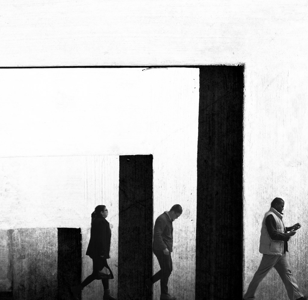 The image shows three people walking against a plain, white background with three vertical, thick, black bars of differing heights. The first person, a woman, is walking past the shortest bar. The second person, a man, walks past the middle-height bar. The third person, another man, is walking and reading a small book or device, in front of the tallest bar.